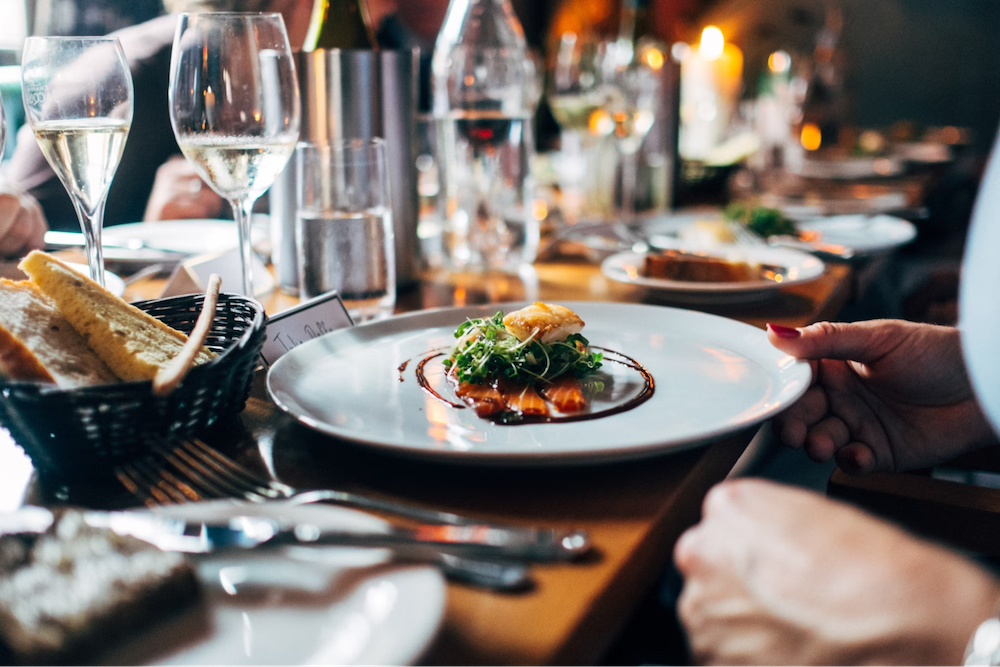 People are at a restaurant, with plates of stunning food placed in front of them.