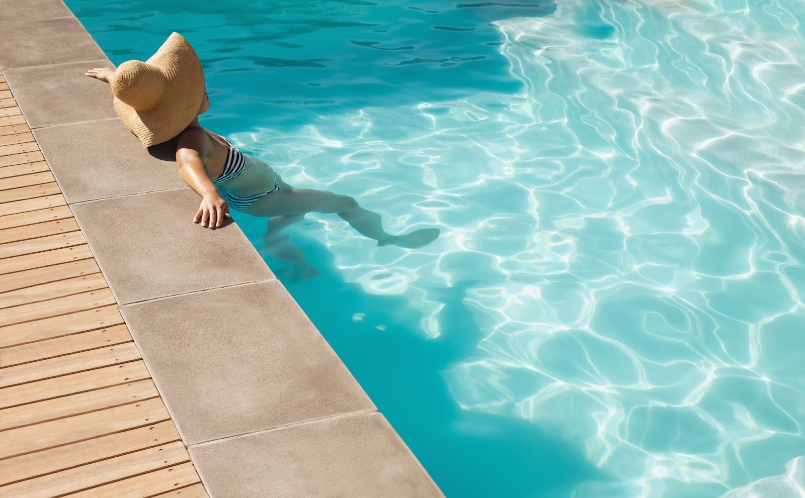 Woman in a sunhat relaxing on the edge of a pool on a sunny day