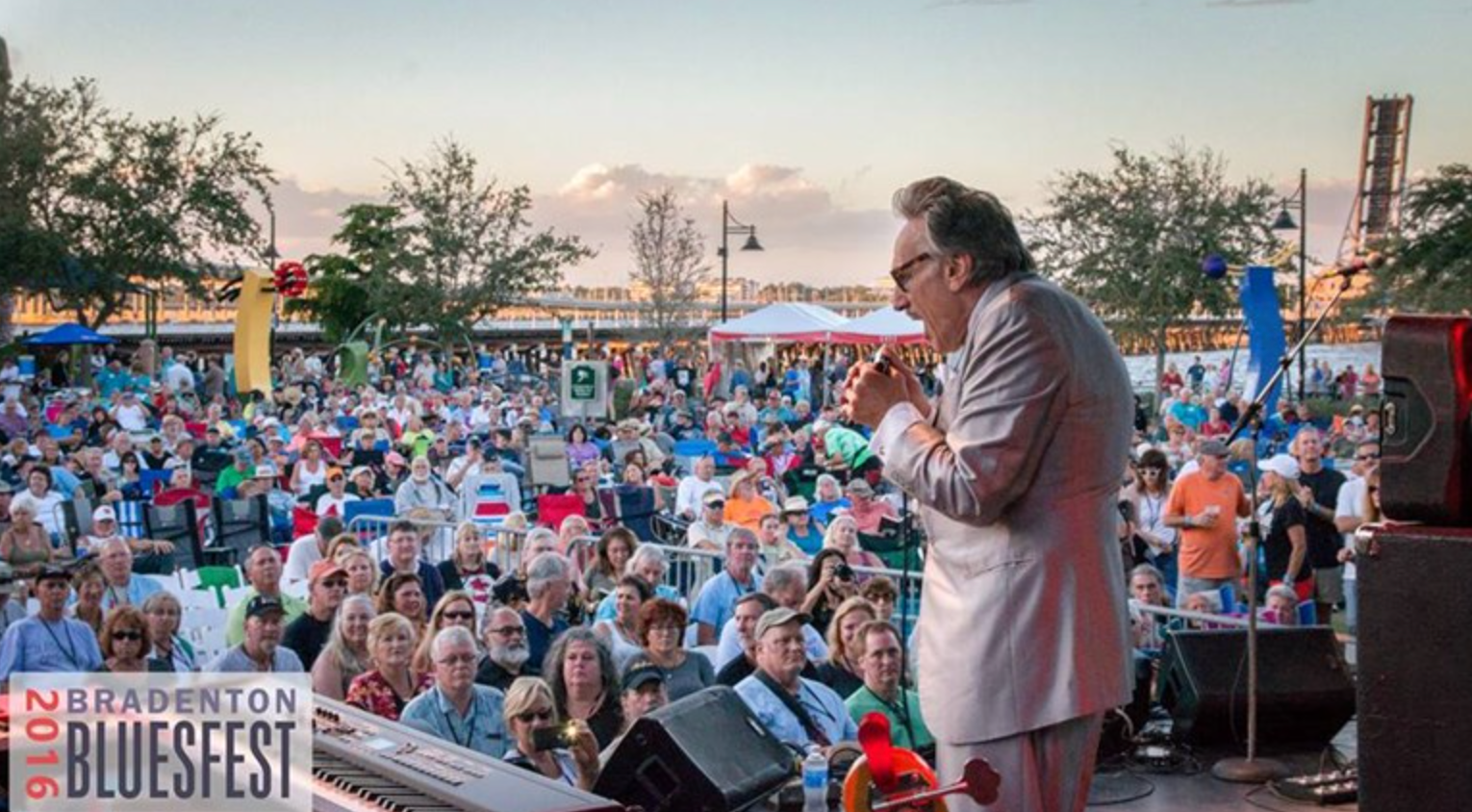 Man singing and performing on an outdoor stage to a crowd of people