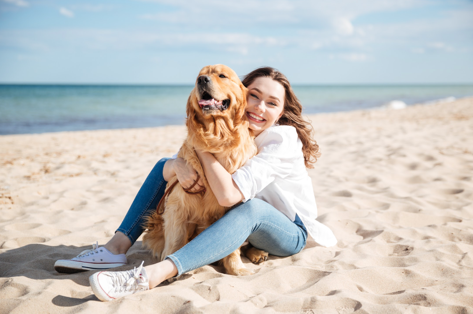 Happy woman sitting and hugging her dog on the beach 
