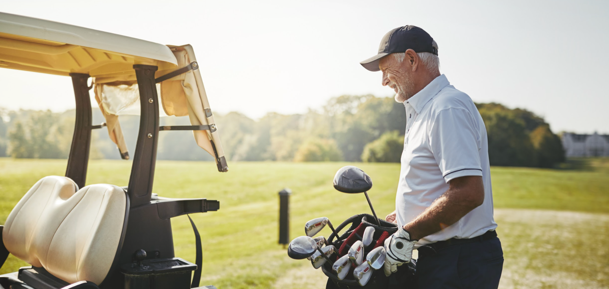 Senior man putting his golf club bag on a cart 