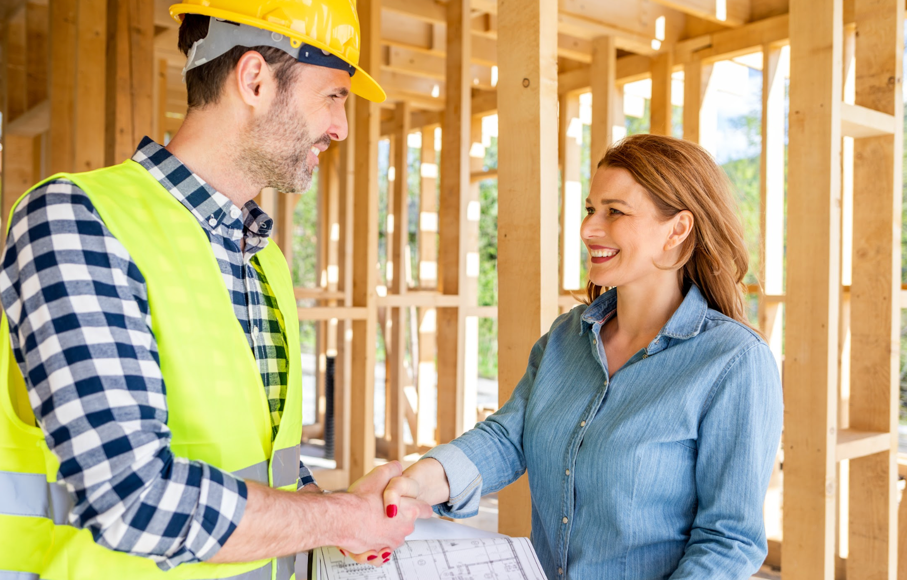 Builder on construction site of new house shaking hands with homeowner