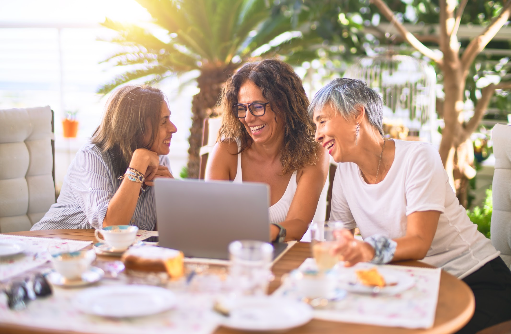 Mature friends smiling happy using laptop at home on a sunny day.