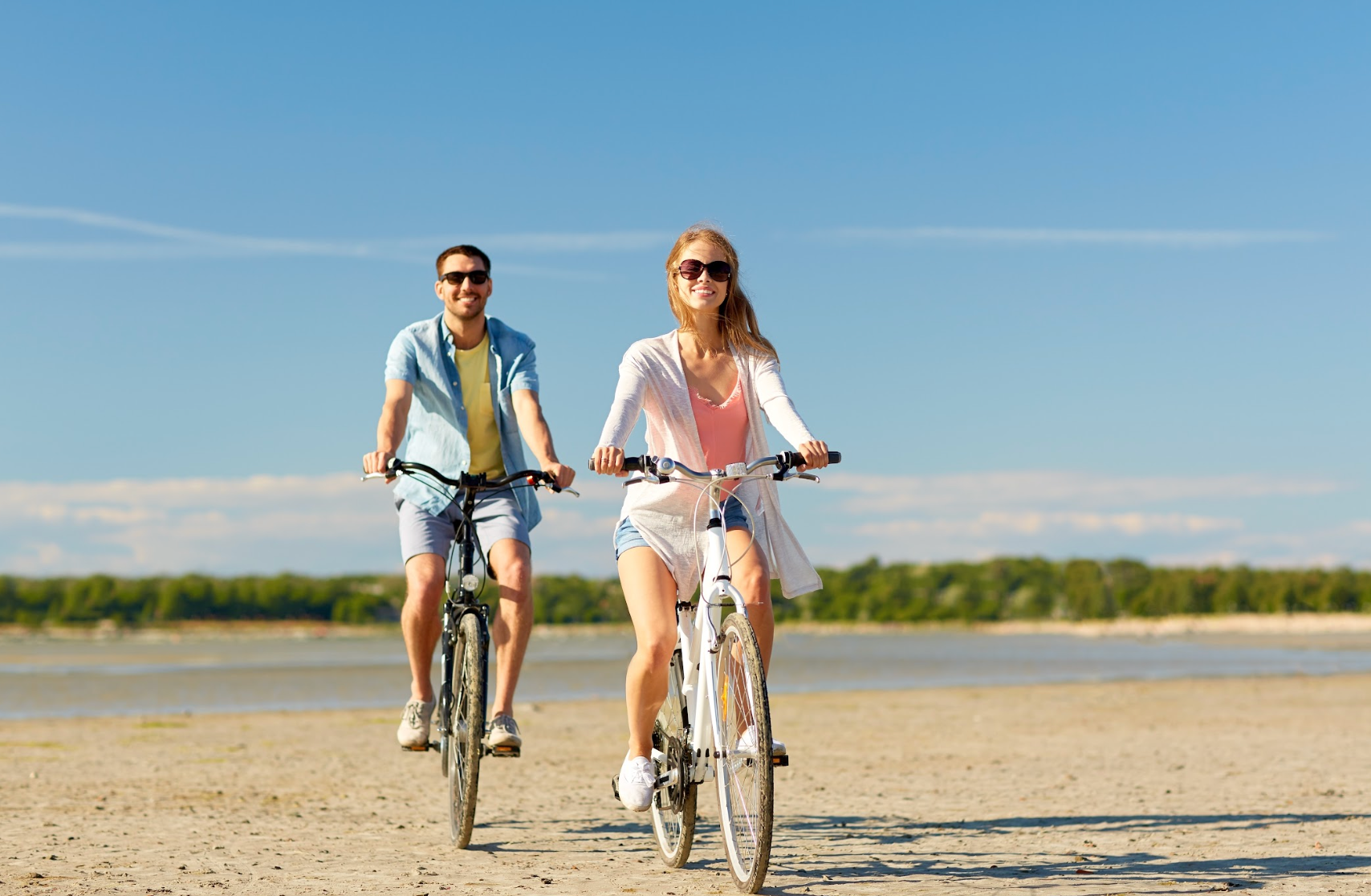 Happy couple with bicycles riding along the shore