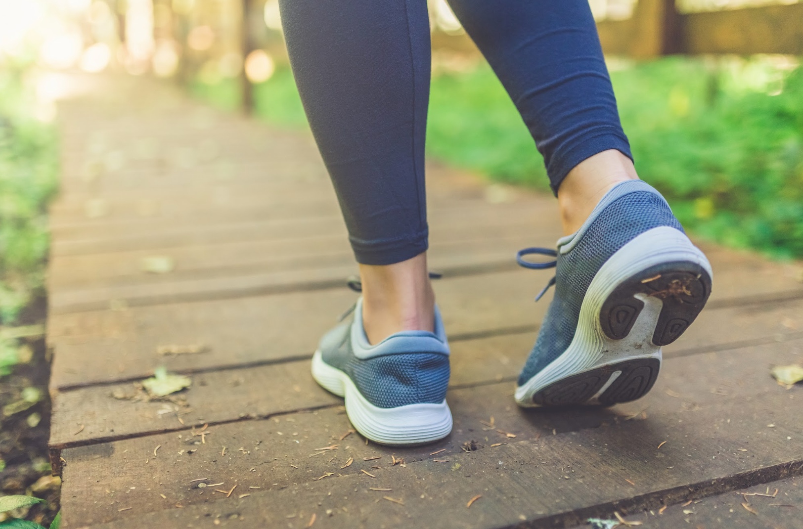 Close up of woman walking on a boardwalk nature trail in tennis shoes.