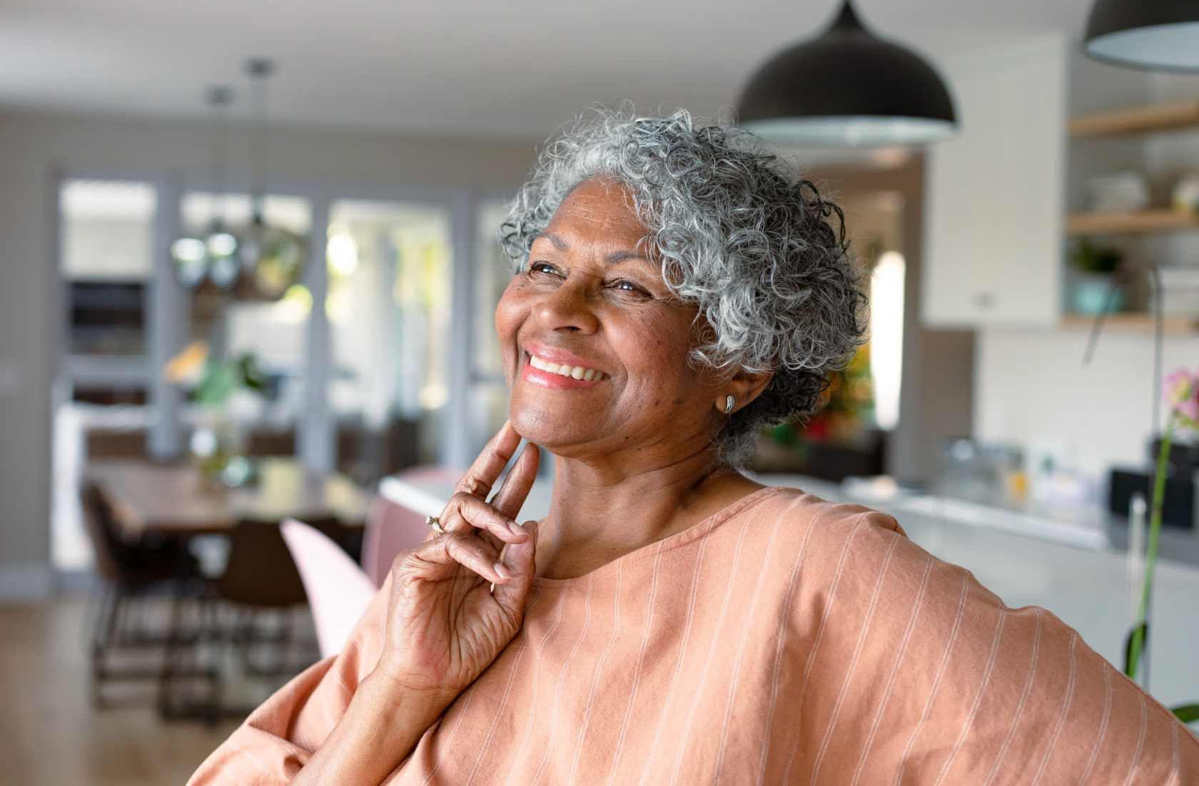 Happy african american senior woman touching face, standing standing in kitchen