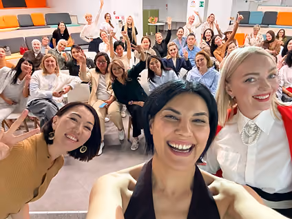 A diverse group of smiling people posing for a cheerful selfie in a modern room with colorful seating.