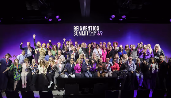 Group photo of diverse attendees at the Reinvention Summit Dublin 2025 on a stage with a purple backdrop.
