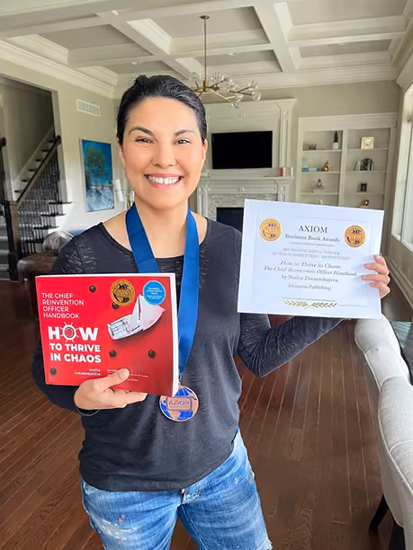 Smiling woman holding a book titled How to Thrive in Chaos and an award certificate indoors.