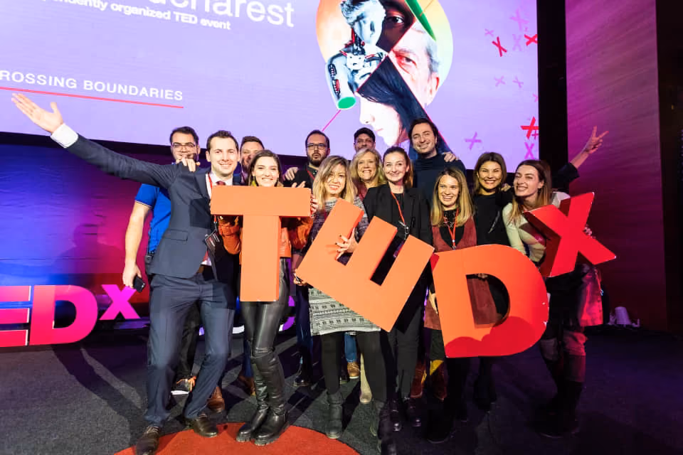 Group of smiling people holding large TEDx letters on stage at a TEDx event.