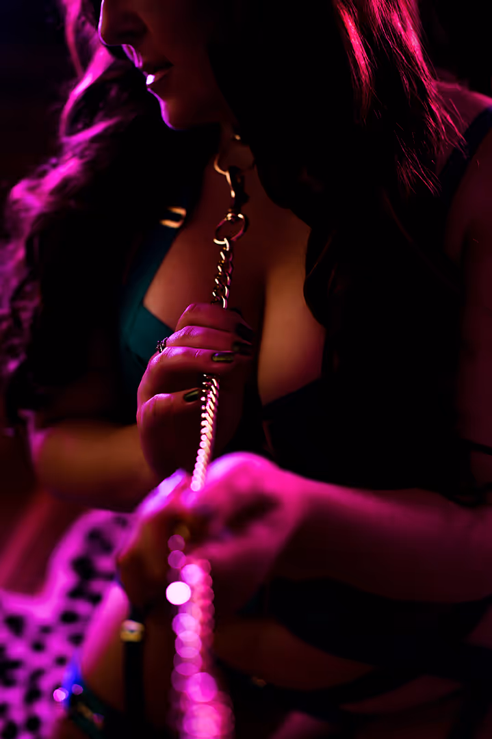 Woman holding a metal chain near her neck, illuminated by pink and purple lighting.
