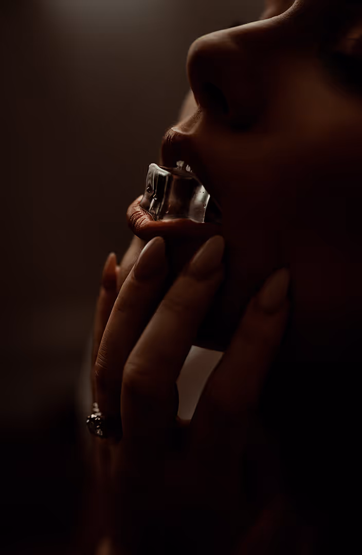 Close-up of a person holding and biting a piece of ice with their lips and fingers in dim lighting.