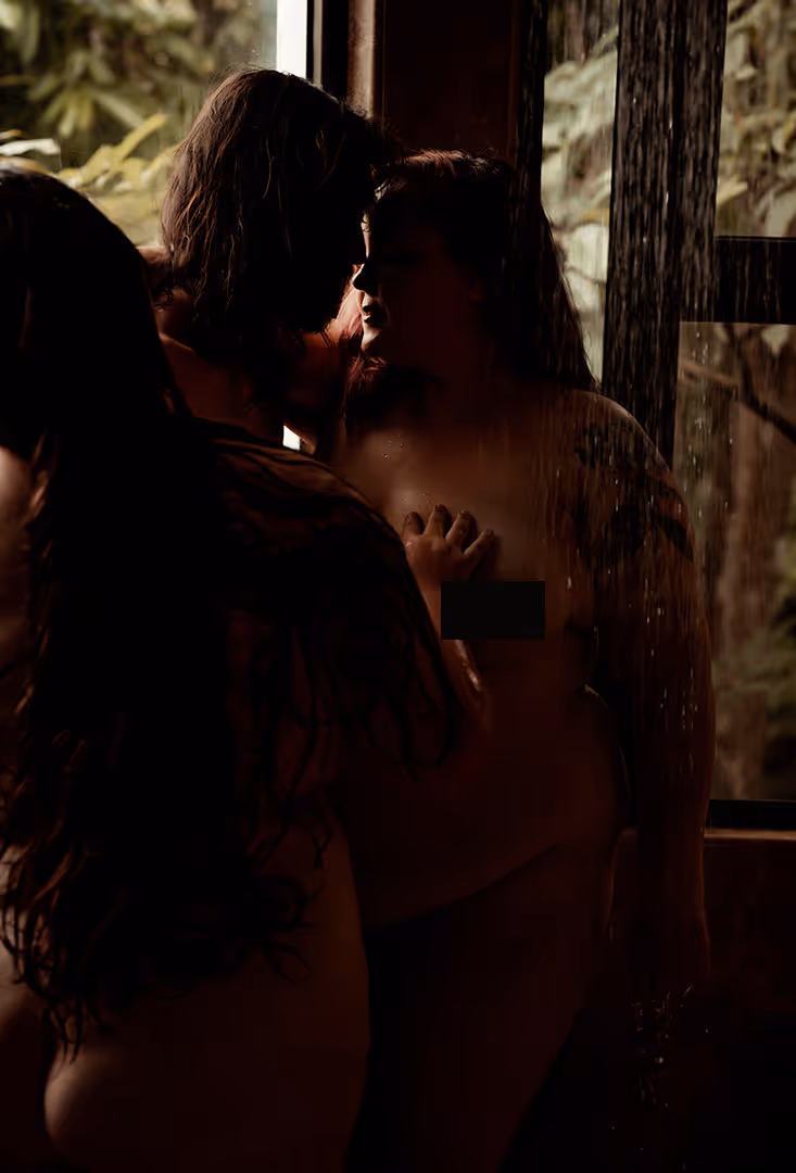 Silhouetted intimate moment between two people in a dimly lit shower with water running.