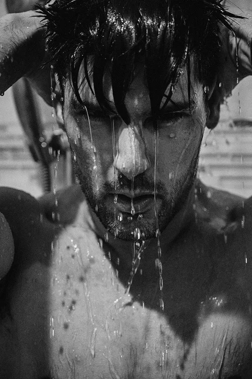 Black and white close-up of a man with wet hair and water droplets running down his face and chest.