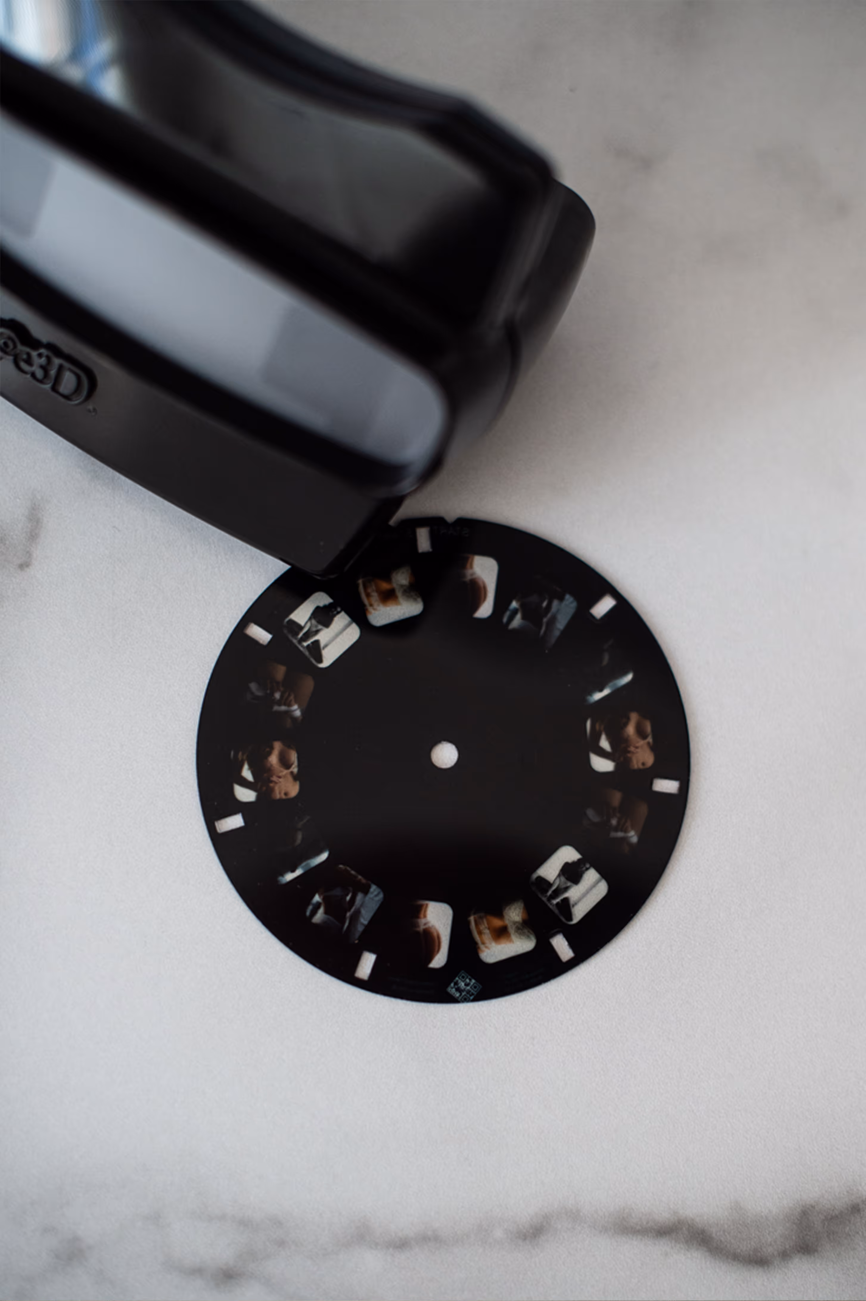 A black View-Master device positioned above a circular photo reel with small images on a marble surface.
