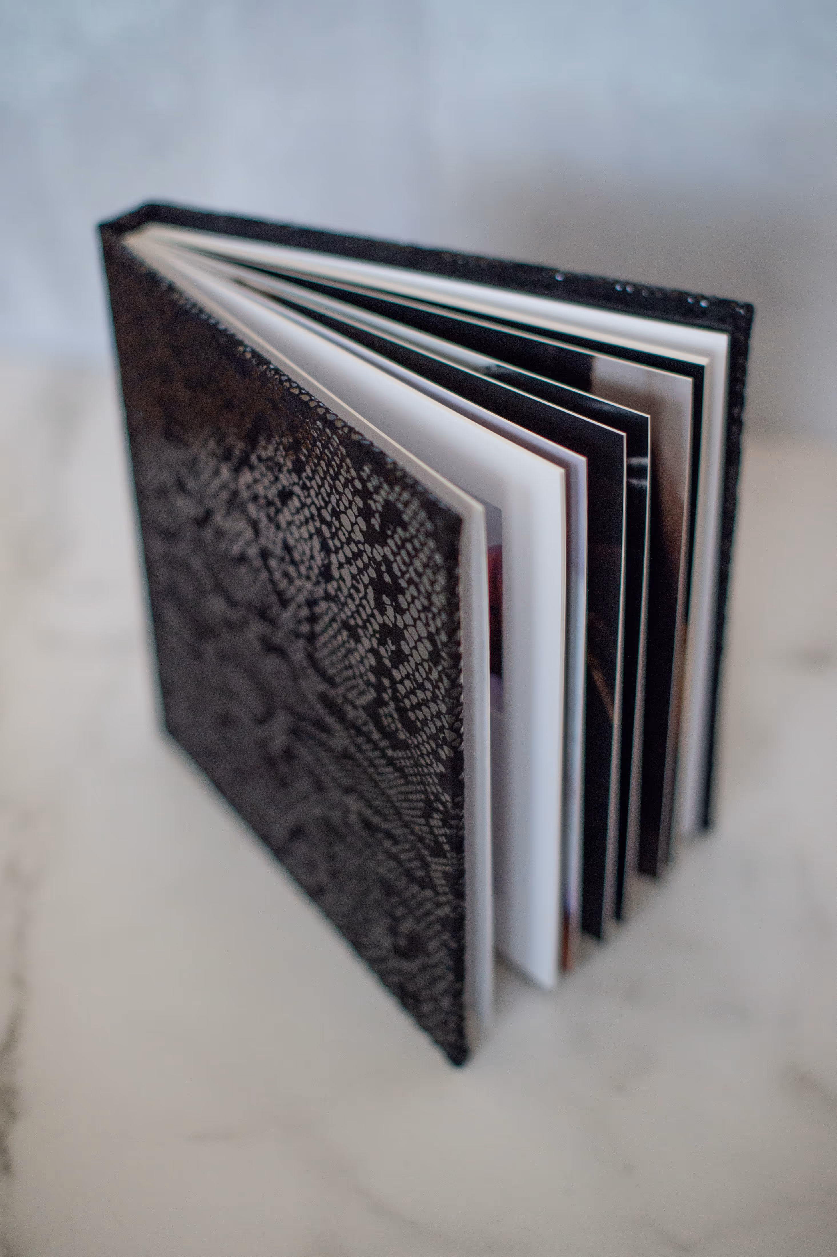 Black photo album with a lace-patterned cover, partially open and standing on a marble surface.