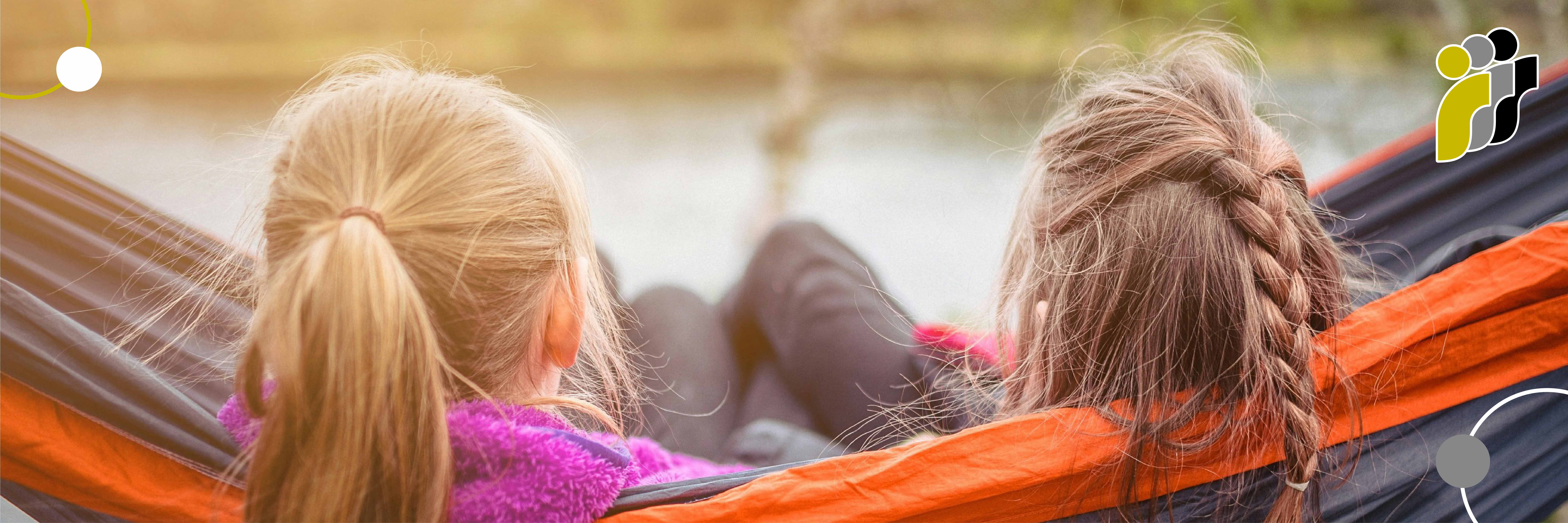 Zwei Kinder mit Zöpfen sitzen zusammen in einer Hängematte am Gewässer.