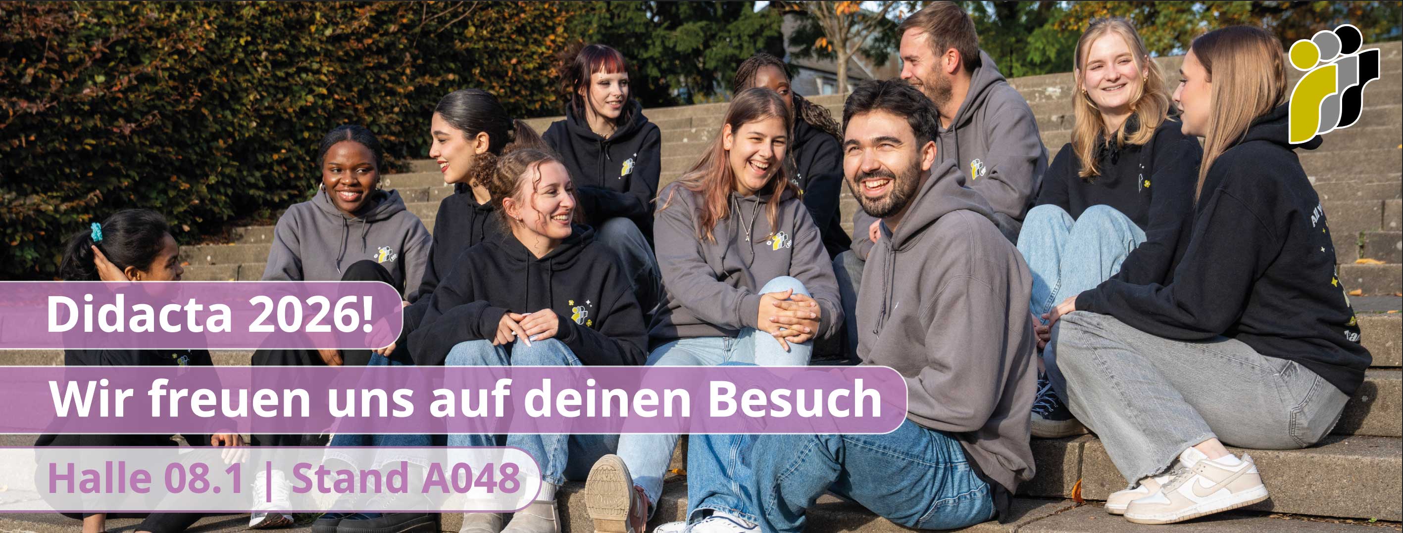 Eine Gruppe von Menschen sitzt auf einer Treppe. Auf dem Bild steht "Didacta 2026! Wir freuen uns auf euren Besuch. Halle 08.1, Stand A048!