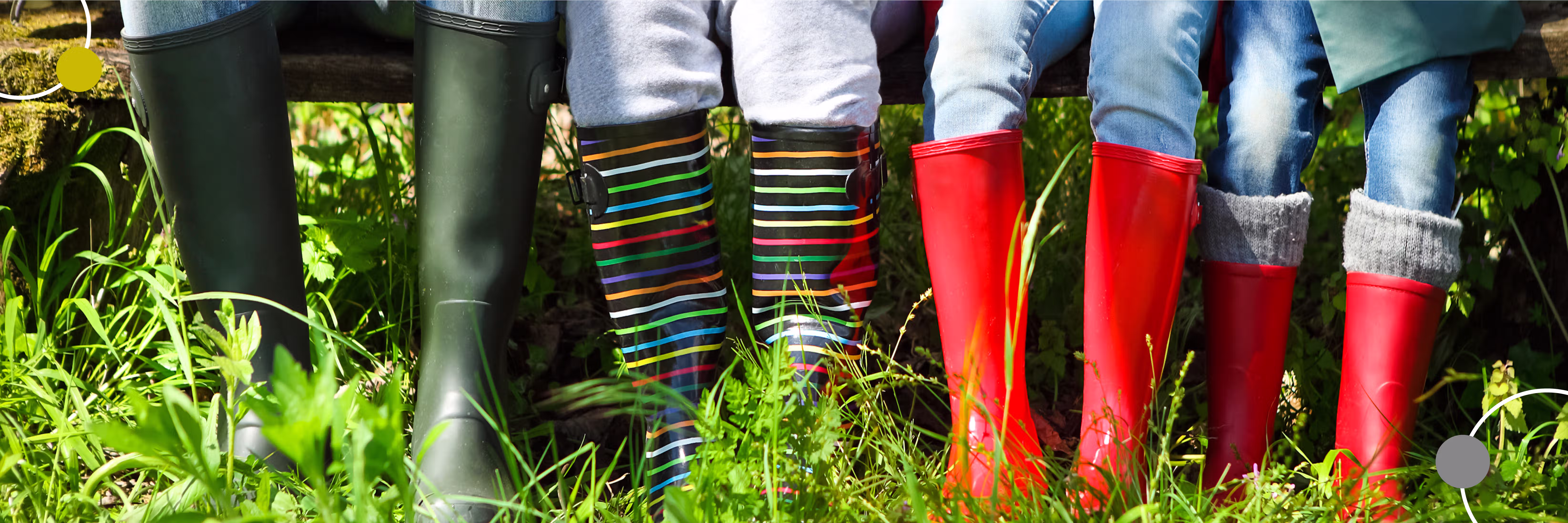 Kinder sitzen auf einer Bank, tragen bunte Gummistiefel in Gras und Natur.