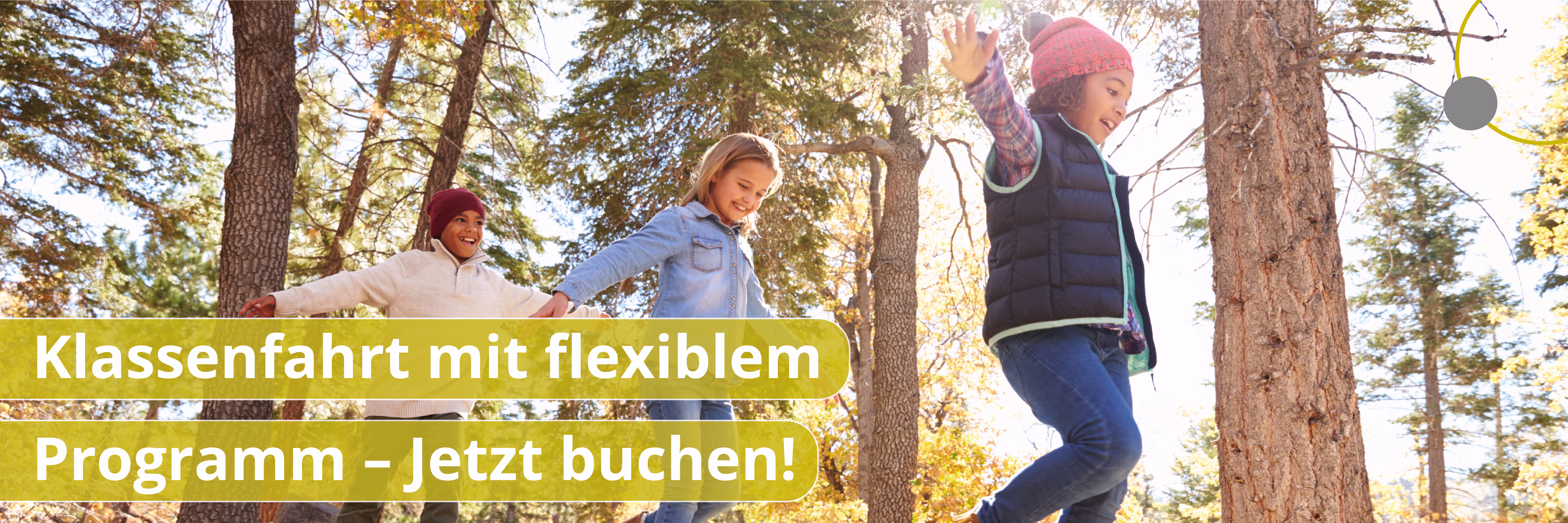 Drei Kinder springen fröhlich im Wald mit Herbstlaub, ein Mädchen trägt bunte Mütze.