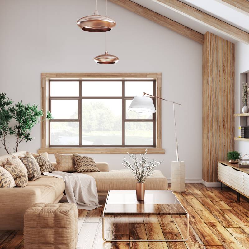Bright living room with light beige sectional sofa adorned with patterned cushions, a glass coffee table with a flower vase, wooden floor, large window, and modern pendant and floor lamps.