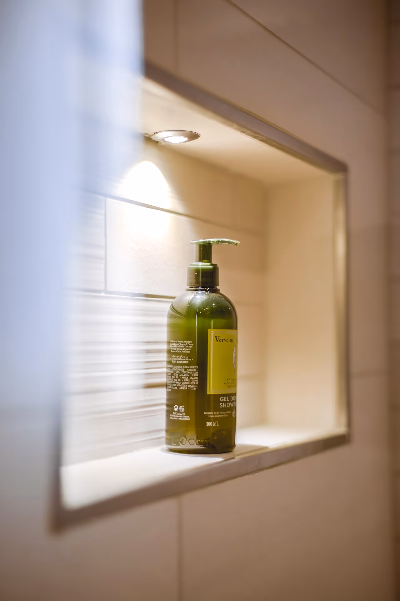 A luxury shower niche with spotlight accents and premium bath products displayed on a glass shelf.