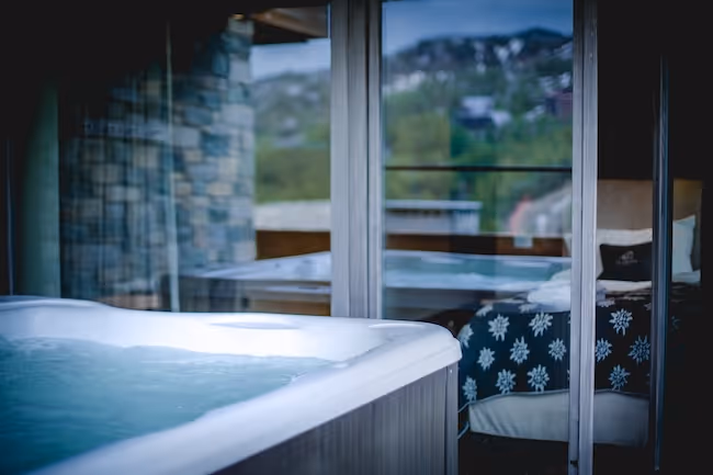 Uitzicht vanuit de jacuzzi op een sfeervolle slaapkamer met warme houten accenten en een sneeuwvlokpatroon op het beddengoed.