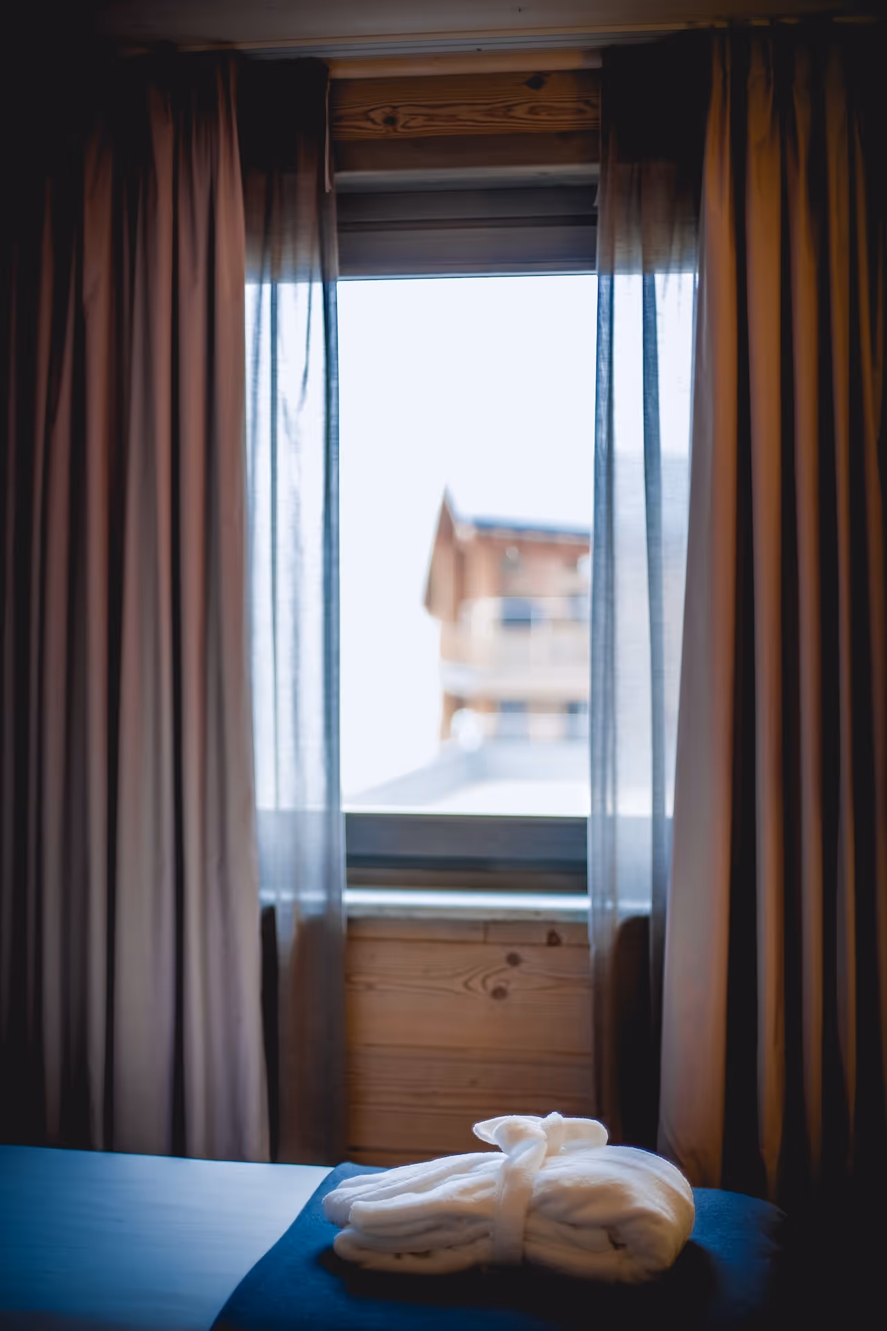 Soft curtains framing a scenic view of an alpine chalet from the Master Suite’s window.