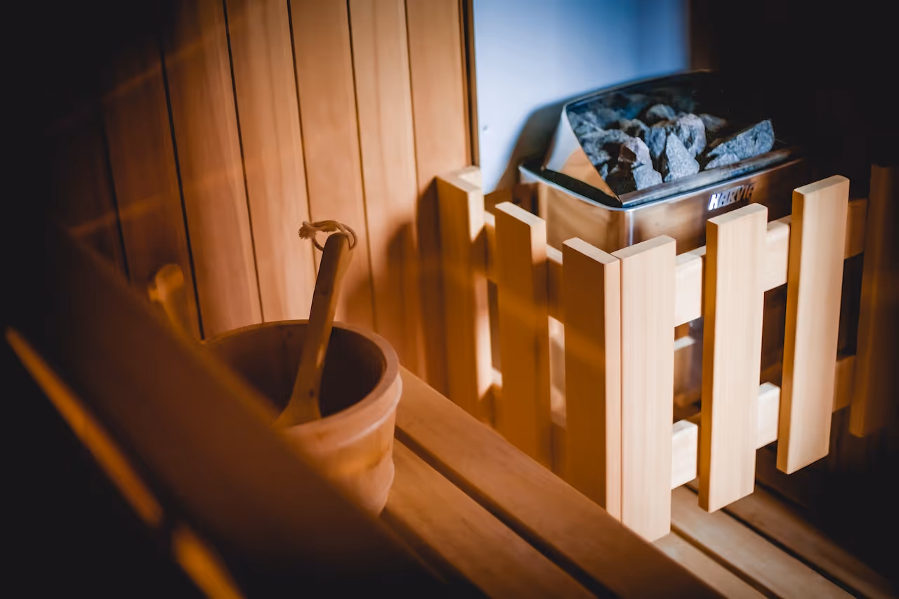 Traditional wooden sauna bucket and ladle beside heated stones, creating a relaxing atmosphere.