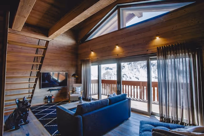 Ruime woonkamer met houten interieur en grote ramen die een panoramisch uitzicht bieden.