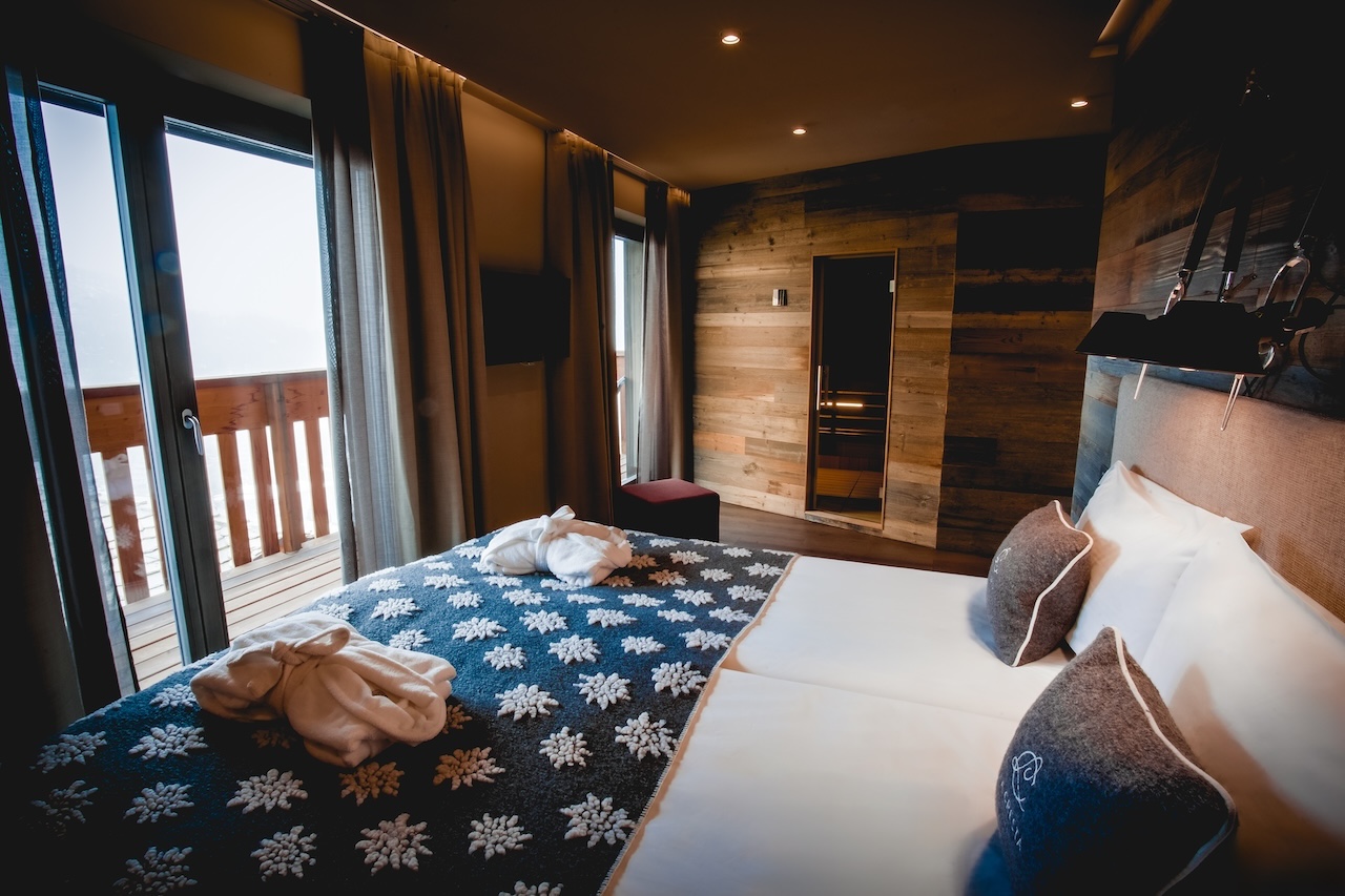 King-size bed with snowflake-patterned blanket and folded bathrobes in the Snow Spa Room at La Cresta, with a private sauna and doors opening onto a wooden terrace.