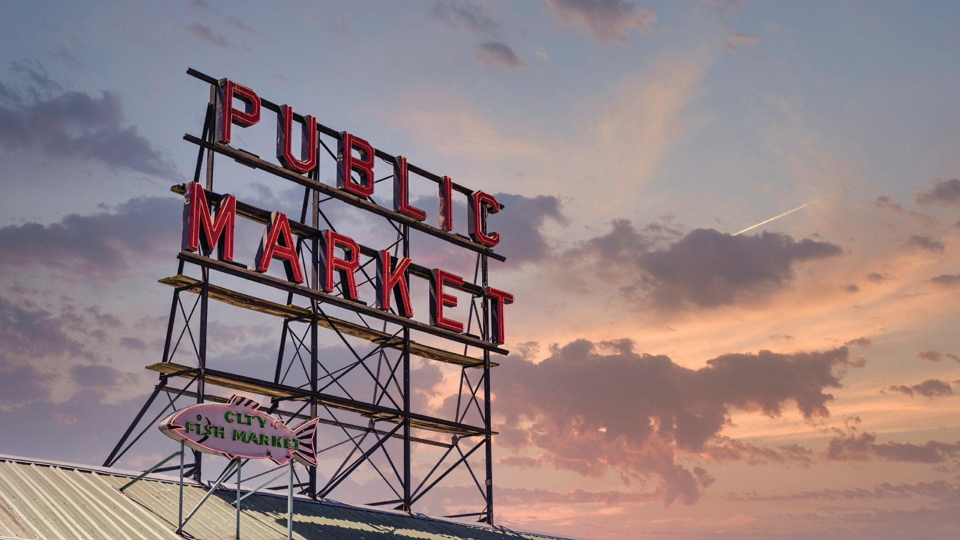Large neon sign reading 'PUBLIC MARKET' with a smaller fish-shaped sign saying 'CITY FISH MARKET' against a colorful sunset sky.