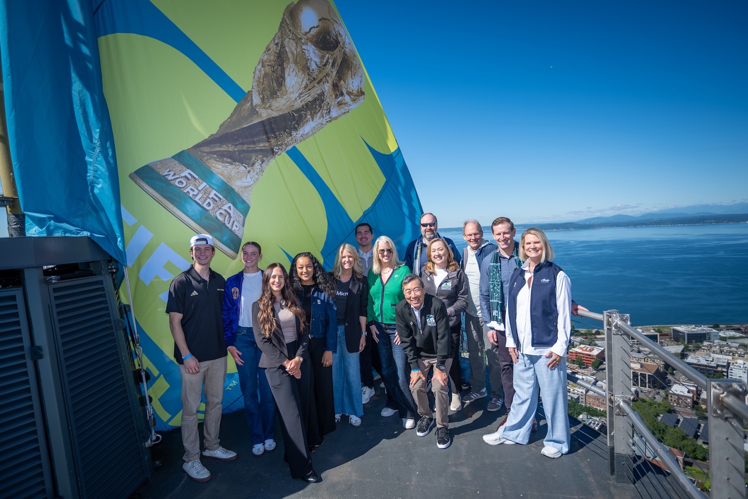 Group of people on top of the Space Needle raising the Seattle FIFA flag.