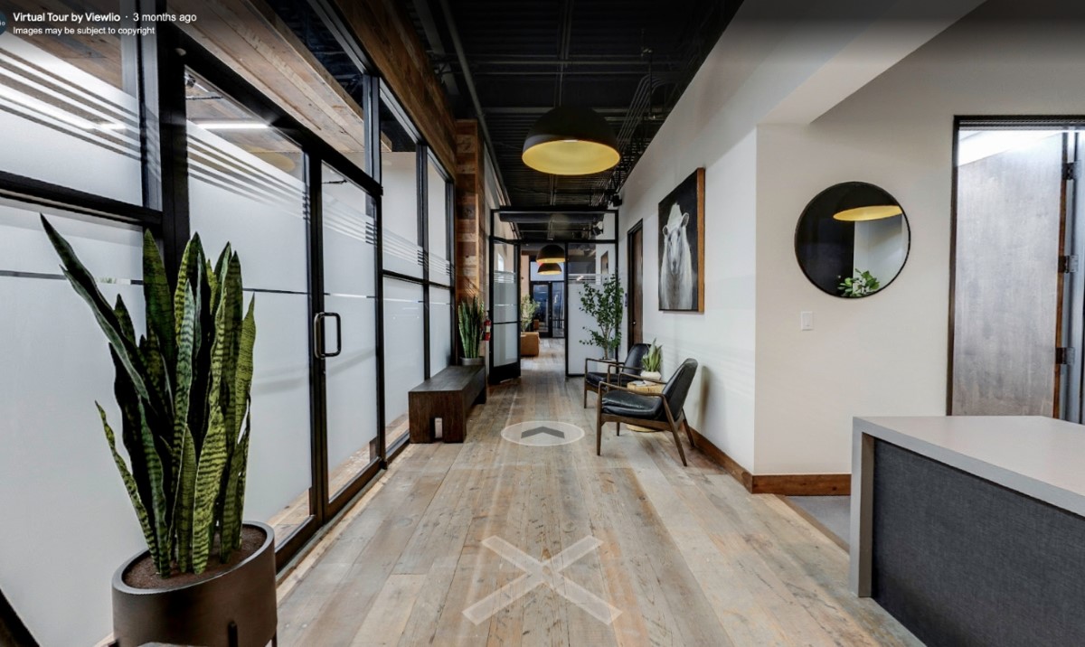 Lucid office corridor with wooden floors, potted plants, black leather chairs, pendant lighting, and frosted glass walls