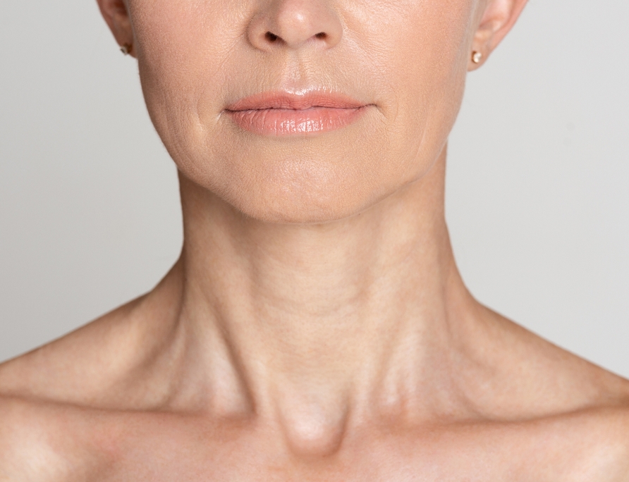 Close-up of a woman's lower face, neck, and upper shoulders with smooth skin and light makeup on lips.