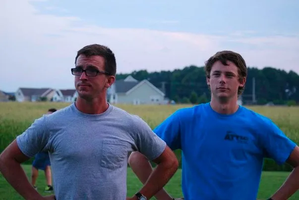 An old photo of two of the founders of Peartree Web Development with hands on hips stand outdoors in front of fields and houses at dusk.