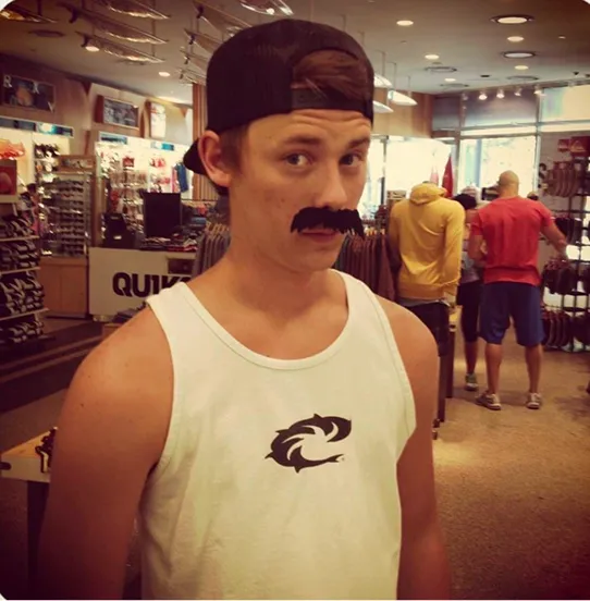 An old photo of one of the founders of Peartree Web Development in white tank top and black cap wearing a fake mustache inside a store.