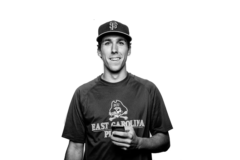 Old photo of one of the founders of Peartree smiling, holding a phone, wearing an ECU shirt