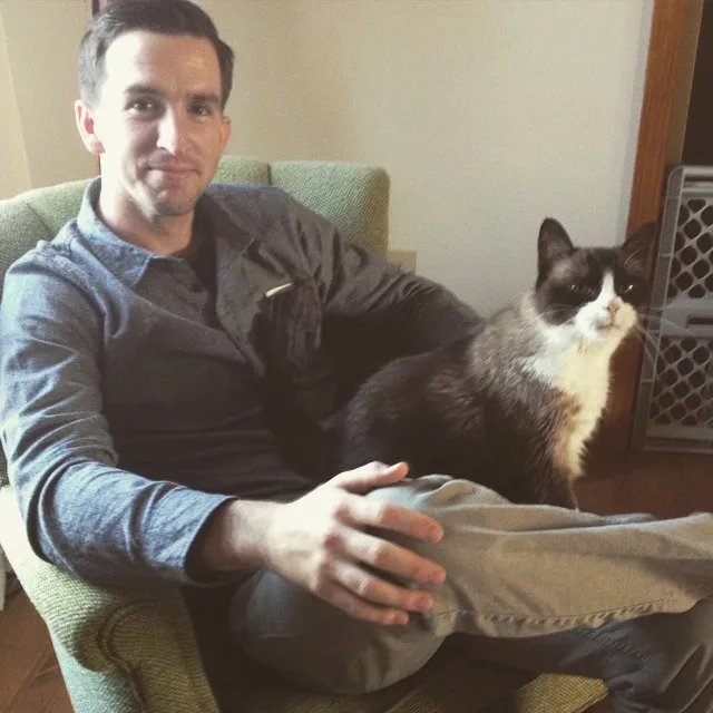 Old photo of one of the founders of Peartree sitting in a green chair with a black and white cat on his lap.