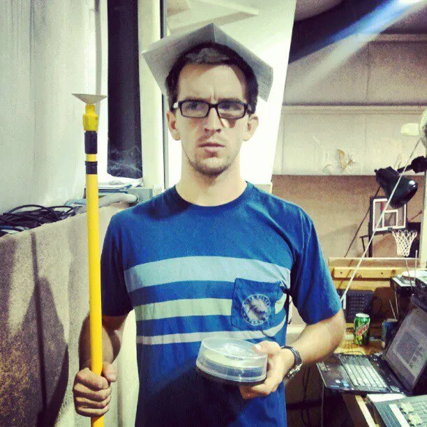 Old photo of one of the founders of Peartree Web Development wearing paper hat holding a yellow pole and CDs in a cluttered room with tech gear.