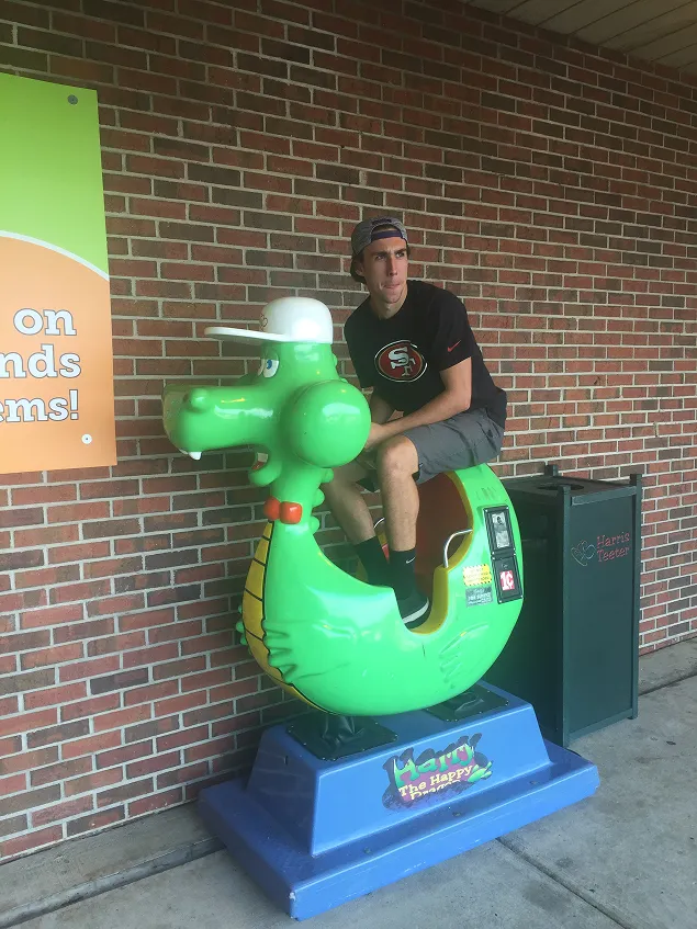 Old photo of one of the founders of Peartree Web Development wearing a 49ers shirt sitting on a green kiddie ride shaped like a dragon.