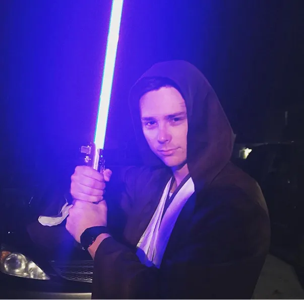 One of the Founders of Peartree Web Development in dark hooded robe holding a glowing blue lightsaber at night.