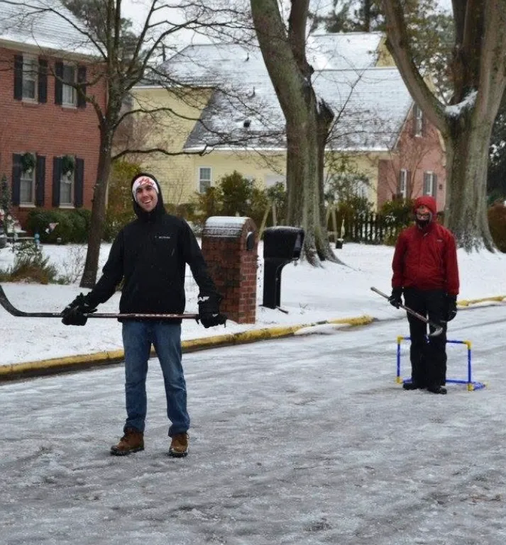 Old photo of the founders of Peartree holding hockey sticks on a snow-covered residential street with trees and houses.