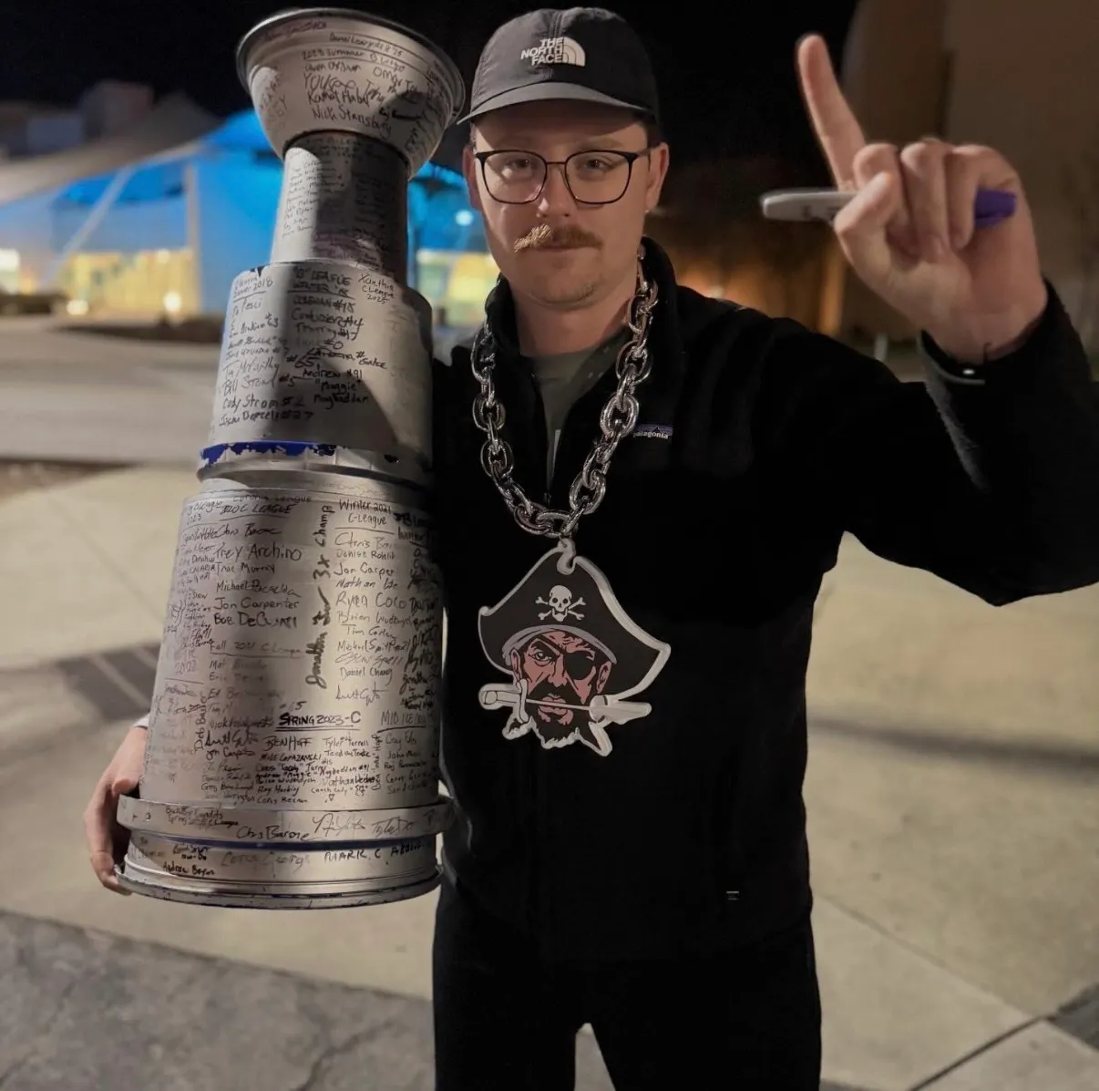 Old photo of one of the founders of Peartree wearing glasses and hat holding a large trophy covered in signatures and wearing a pirate medallion.