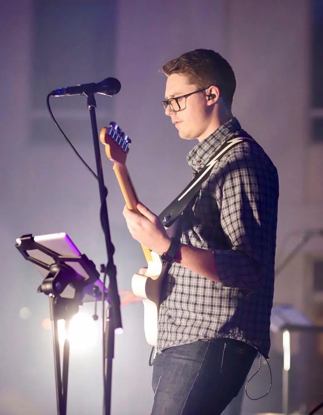 Old photo of one of the founders of Peartree playing electric guitar and singing into a microphone on stage.