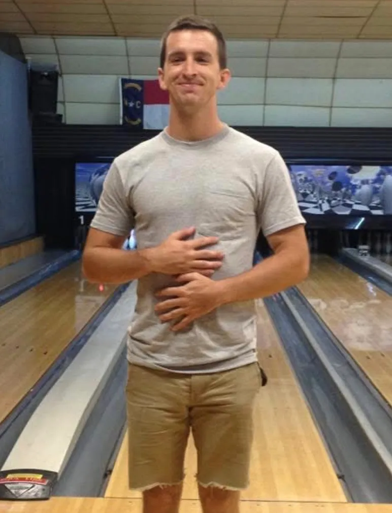 Old photo of one of the founders of Peartree standing and smiling in a bowling alley between two lanes, wearing a gray shirt and khaki shorts.