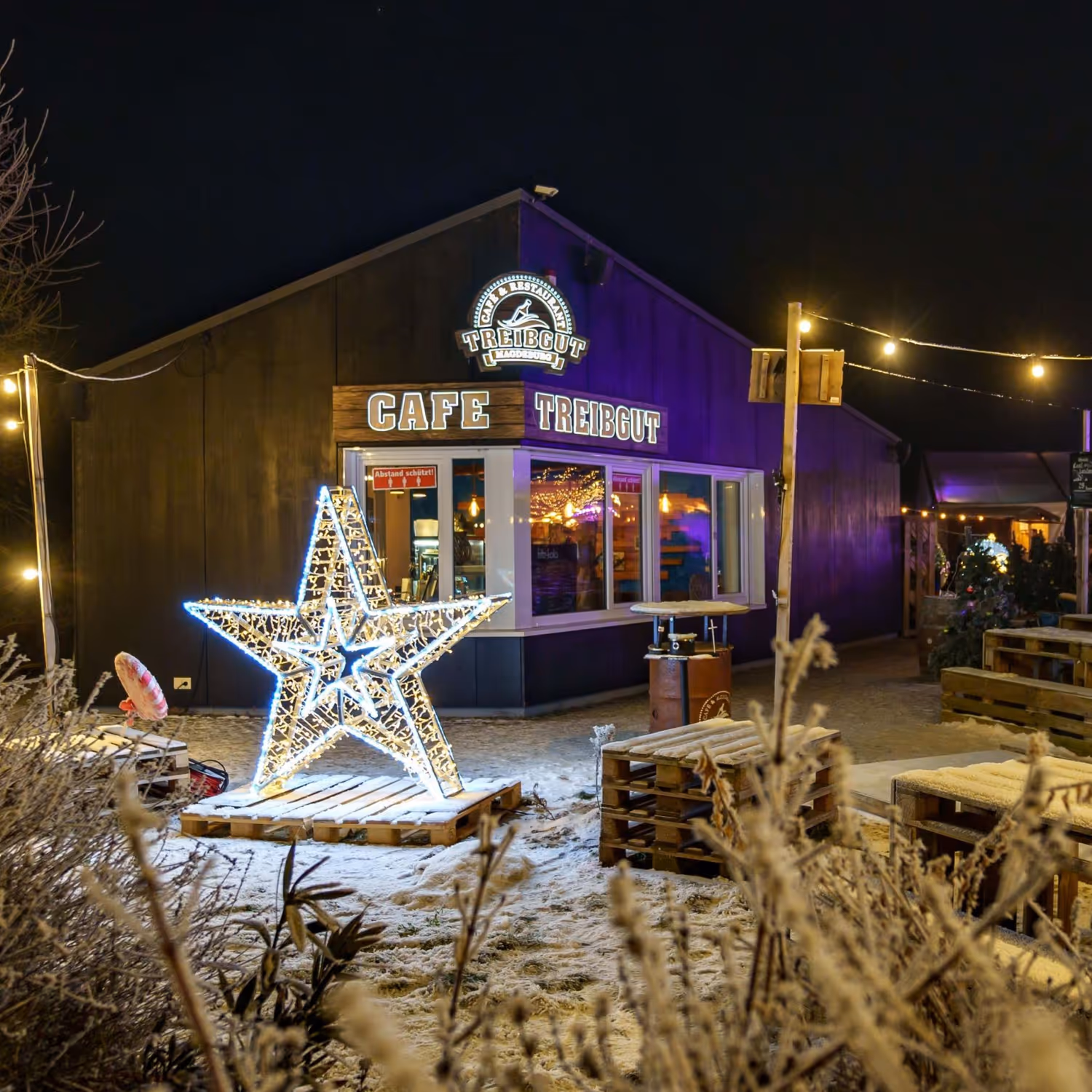 Nachtansicht des Cafe Treibgut Magdeburg mit leuchtendem Stern und Schnee – ideale Location für winterliche Weihnachtsfeiern in Magdeburg.