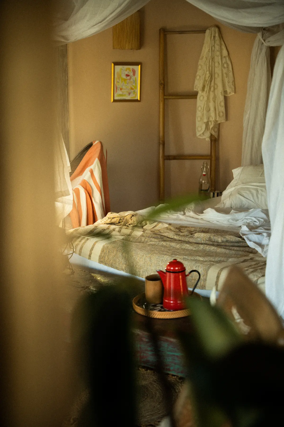 View of a bed with a coffee pot and mug in front. 