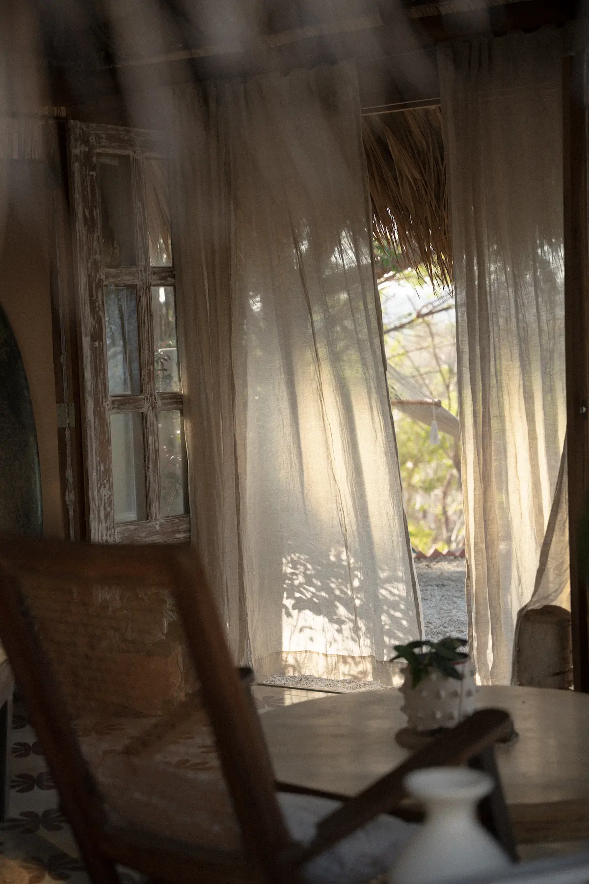 Curtains blowing in the distance and a rocking chair in the foreground.