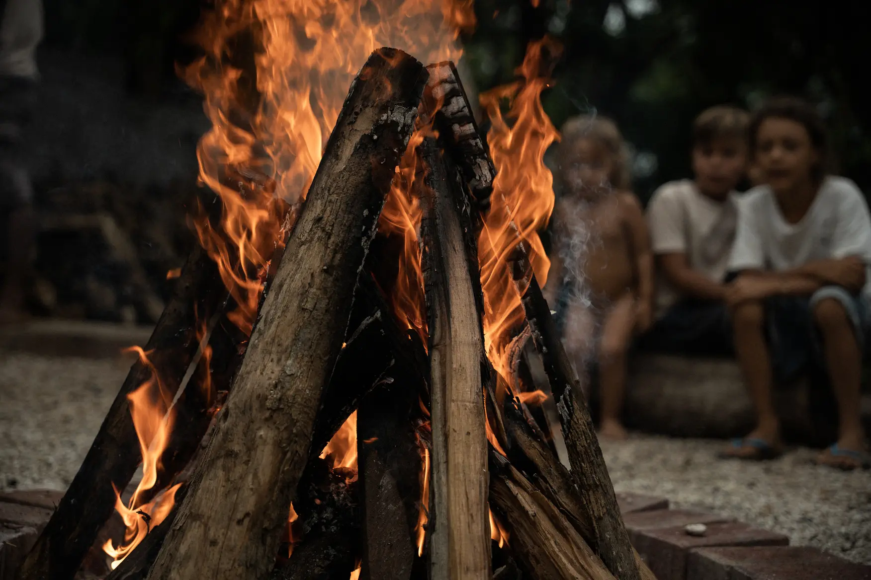 A camp fire with children entranced by the flames.